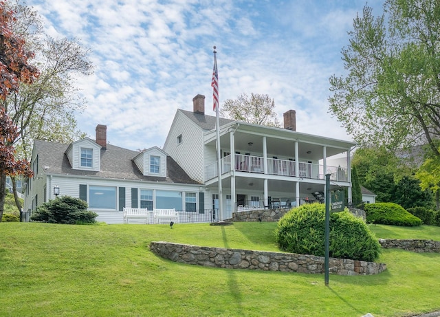 back of property with a balcony, a lawn, and a chimney