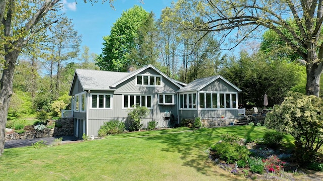 back of property with roof with shingles, a lawn, a sunroom, and a chimney