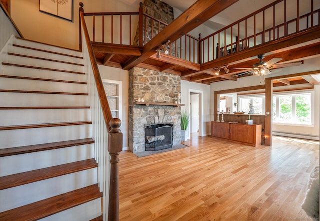 unfurnished living room with light wood finished floors, beamed ceiling, stairs, baseboard heating, and a stone fireplace