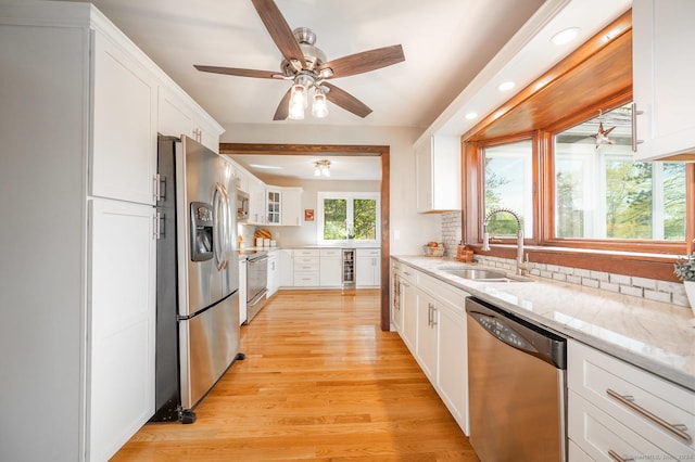 kitchen with light stone countertops, light wood-style flooring, a sink, stainless steel appliances, and white cabinetry