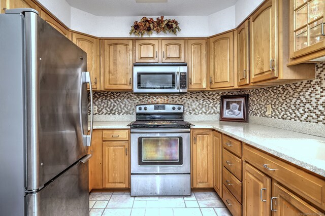 kitchen featuring light stone countertops, appliances with stainless steel finishes, tasteful backsplash, and light tile patterned floors