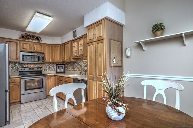 kitchen featuring appliances with stainless steel finishes, a textured ceiling, tasteful backsplash, and sink