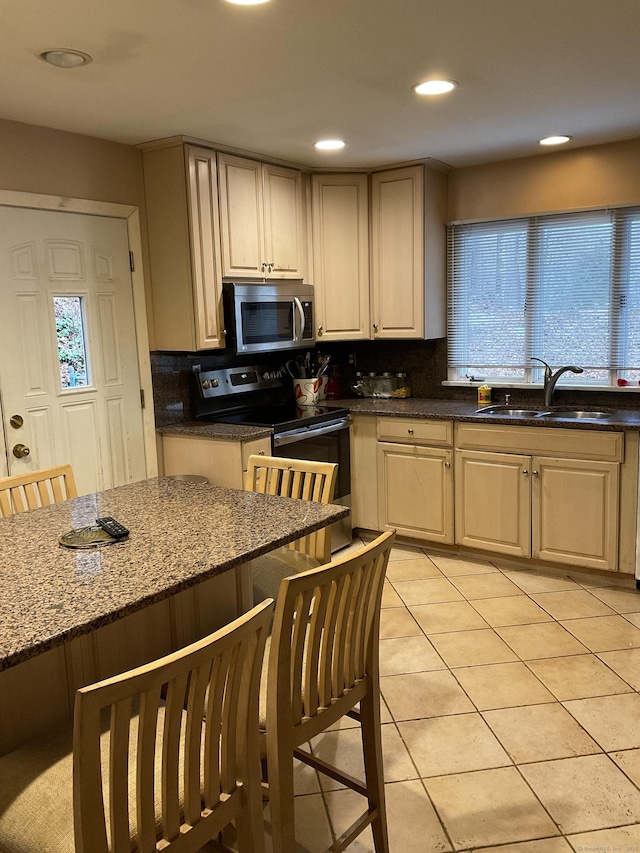 kitchen with appliances with stainless steel finishes, tasteful backsplash, dark stone counters, sink, and light tile patterned floors