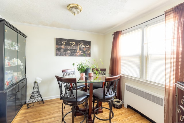 dining room featuring a textured ceiling, light hardwood / wood-style flooring, radiator, and ornamental molding