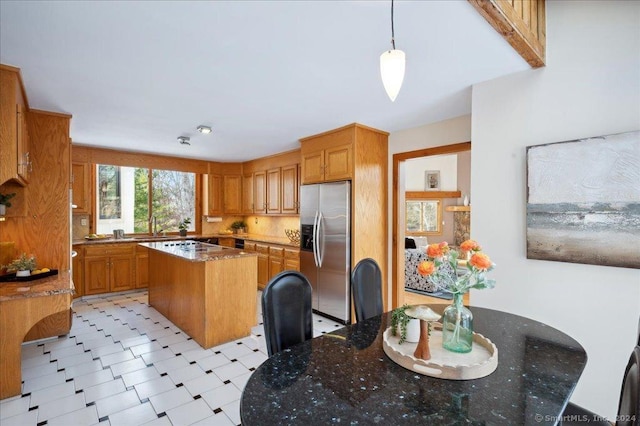 kitchen featuring a center island, hanging light fixtures, stainless steel fridge with ice dispenser, dark stone counters, and a breakfast bar