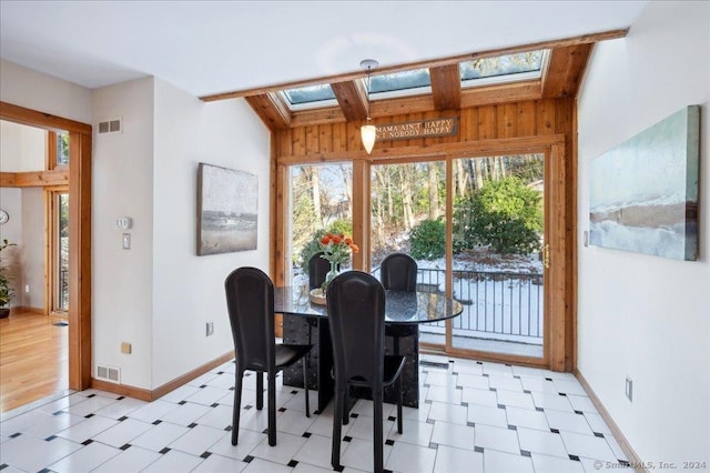 dining room featuring lofted ceiling with skylight and wood walls