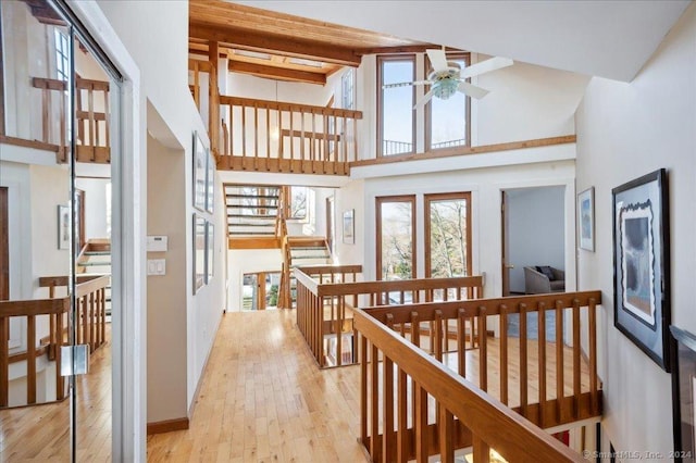 corridor with light hardwood / wood-style floors, beam ceiling, and high vaulted ceiling