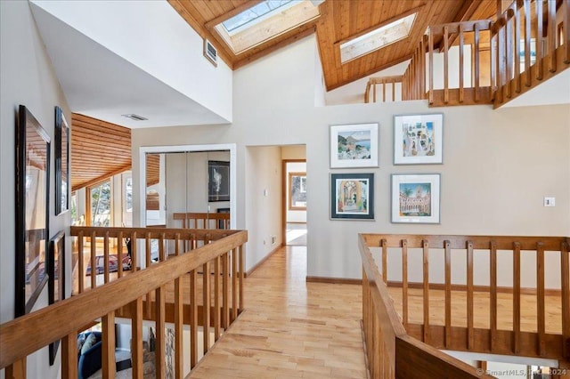 hall with light wood-type flooring, a skylight, high vaulted ceiling, and wood ceiling