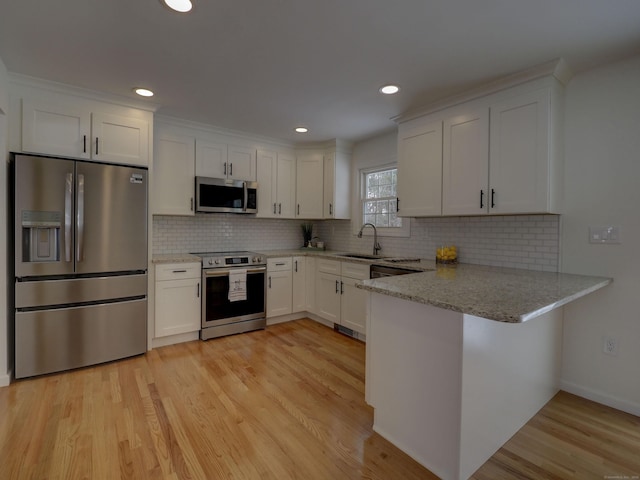 kitchen with white cabinetry, light hardwood / wood-style floors, kitchen peninsula, stainless steel appliances, and light stone countertops