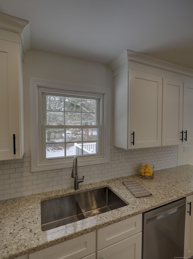 kitchen featuring white cabinetry, sink, stainless steel dishwasher, and light stone countertops