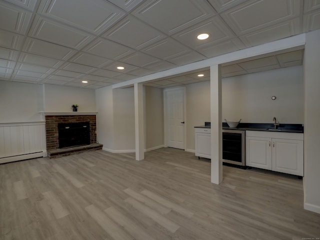 basement featuring a fireplace, beverage cooler, a baseboard heating unit, wet bar, and light wood-type flooring