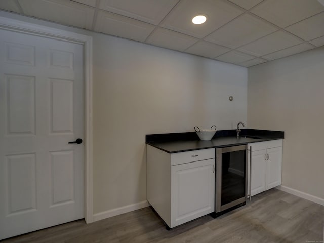 kitchen featuring a paneled ceiling, sink, white cabinets, beverage cooler, and light wood-type flooring