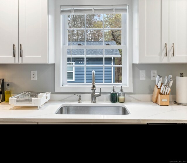 kitchen featuring light stone countertops, white cabinetry, and sink