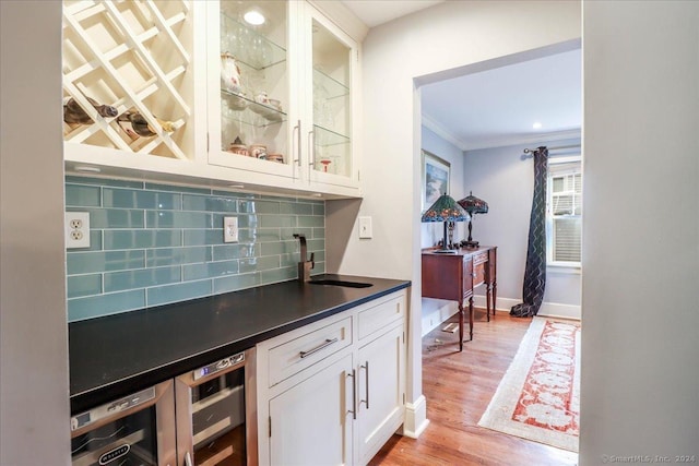 bar featuring light wood-type flooring, tasteful backsplash, ornamental molding, sink, and white cabinets