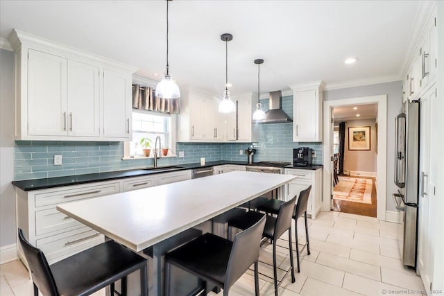 kitchen featuring sink, hanging light fixtures, wall chimney exhaust hood, white cabinetry, and stainless steel appliances