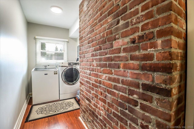 washroom featuring independent washer and dryer, brick wall, and hardwood / wood-style flooring