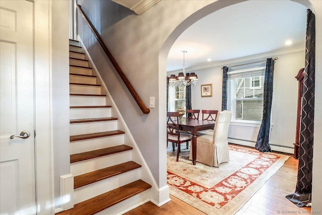 staircase featuring crown molding, hardwood / wood-style floors, a baseboard radiator, and an inviting chandelier