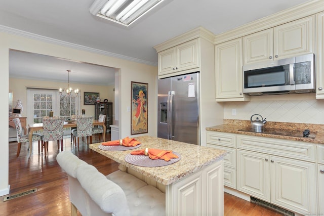 kitchen with cream cabinets, hardwood / wood-style floors, pendant lighting, and appliances with stainless steel finishes