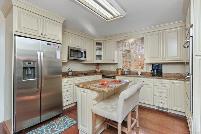 kitchen featuring a center island, a kitchen breakfast bar, dark hardwood / wood-style floors, dark stone countertops, and appliances with stainless steel finishes