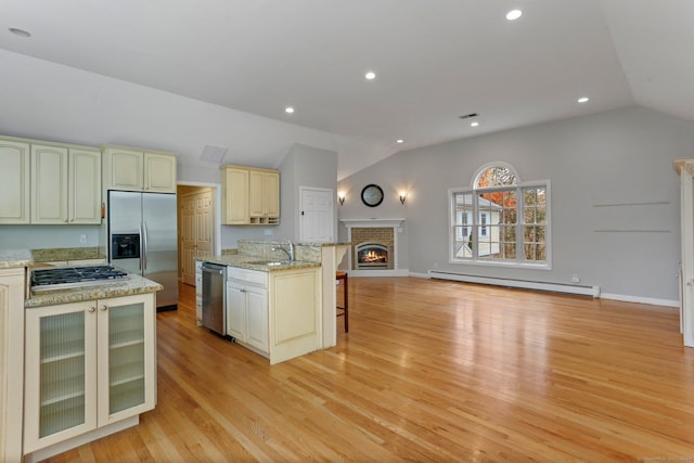 kitchen featuring lofted ceiling, baseboard heating, light hardwood / wood-style floors, light stone counters, and stainless steel appliances