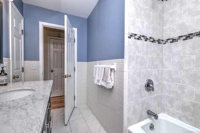 bathroom featuring tiled shower / bath combo, vanity, and tile walls