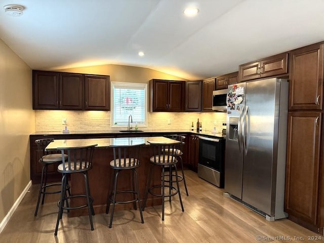 kitchen with lofted ceiling, sink, a breakfast bar area, light hardwood / wood-style flooring, and stainless steel appliances