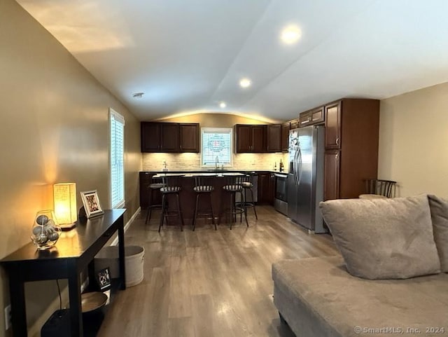 kitchen featuring a breakfast bar, stainless steel appliances, vaulted ceiling, sink, and light hardwood / wood-style flooring