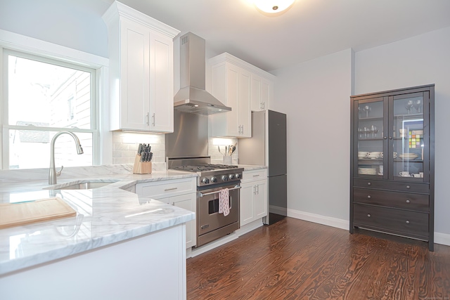 kitchen featuring light stone countertops, wall chimney exhaust hood, high end stainless steel range oven, sink, and white cabinetry