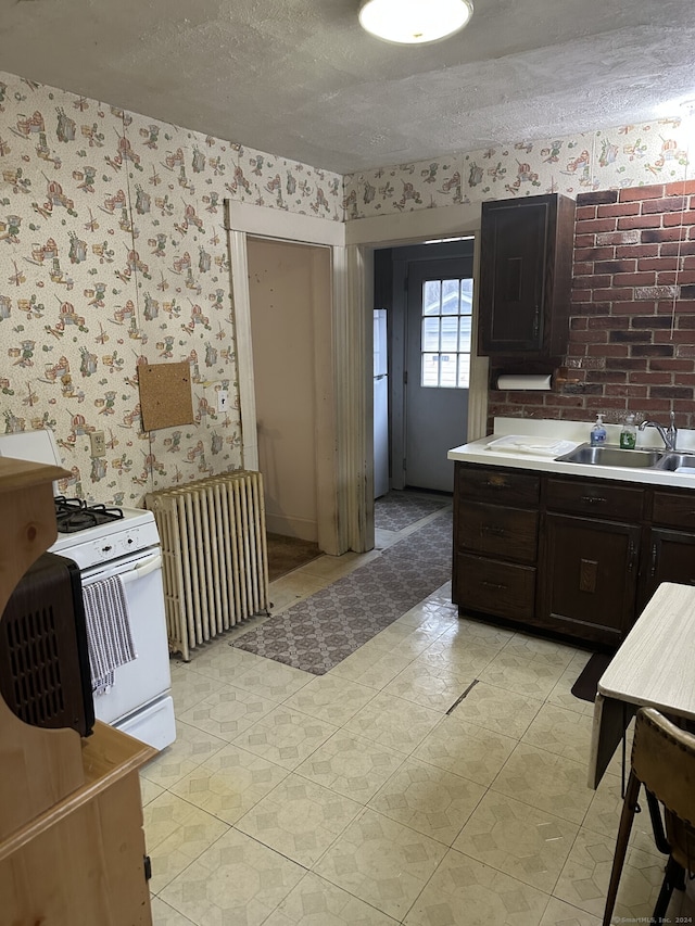 kitchen featuring radiator, sink, white range with gas cooktop, dark brown cabinets, and a textured ceiling