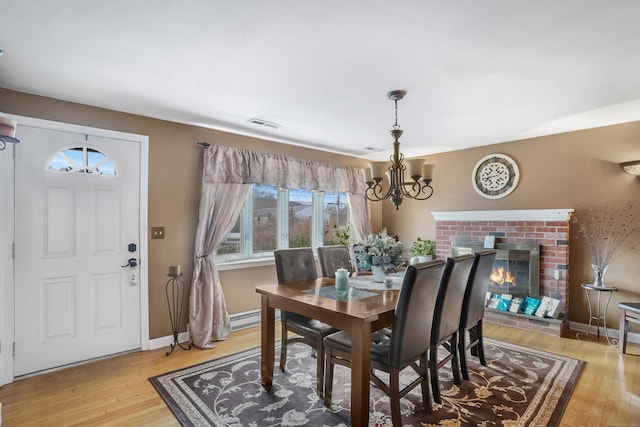 dining room featuring a fireplace, wood-type flooring, a chandelier, and baseboard heating