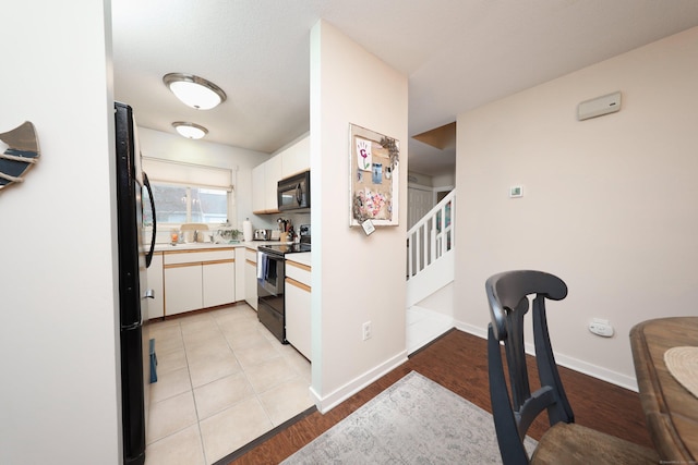 kitchen with white cabinets, black appliances, and light hardwood / wood-style flooring