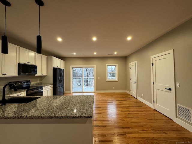 kitchen with hanging light fixtures, dark stone counters, wood-type flooring, white cabinets, and black appliances