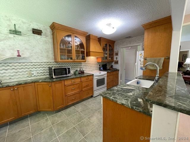 kitchen featuring kitchen peninsula, premium range hood, a textured ceiling, white appliances, and sink