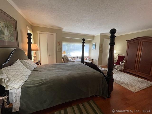 bedroom with a closet, dark wood-type flooring, a textured ceiling, and ornamental molding