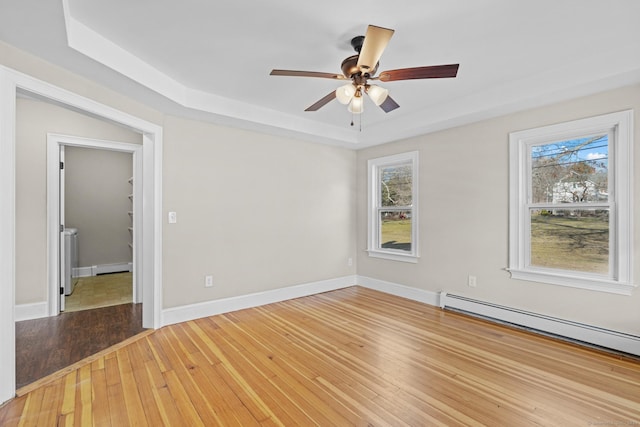 unfurnished room featuring a raised ceiling, plenty of natural light, a baseboard radiator, and hardwood / wood-style flooring