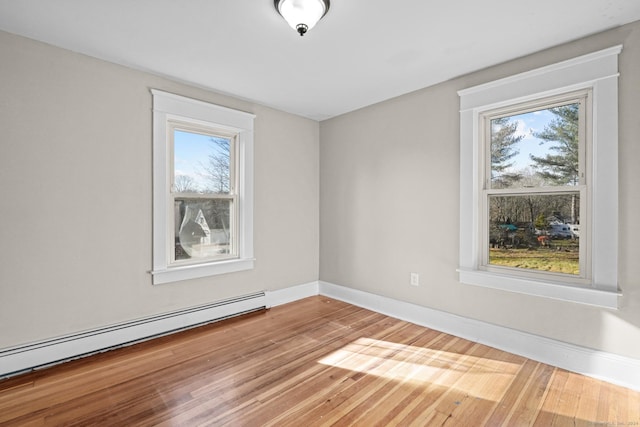 empty room featuring hardwood / wood-style floors, plenty of natural light, and a baseboard heating unit