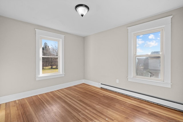 empty room with a wealth of natural light, baseboard heating, and wood-type flooring