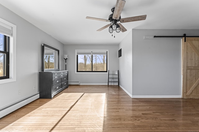 interior space with hardwood / wood-style floors, a barn door, baseboard heating, and a healthy amount of sunlight