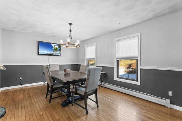 dining area with wood-type flooring, a textured ceiling, a baseboard radiator, and a notable chandelier