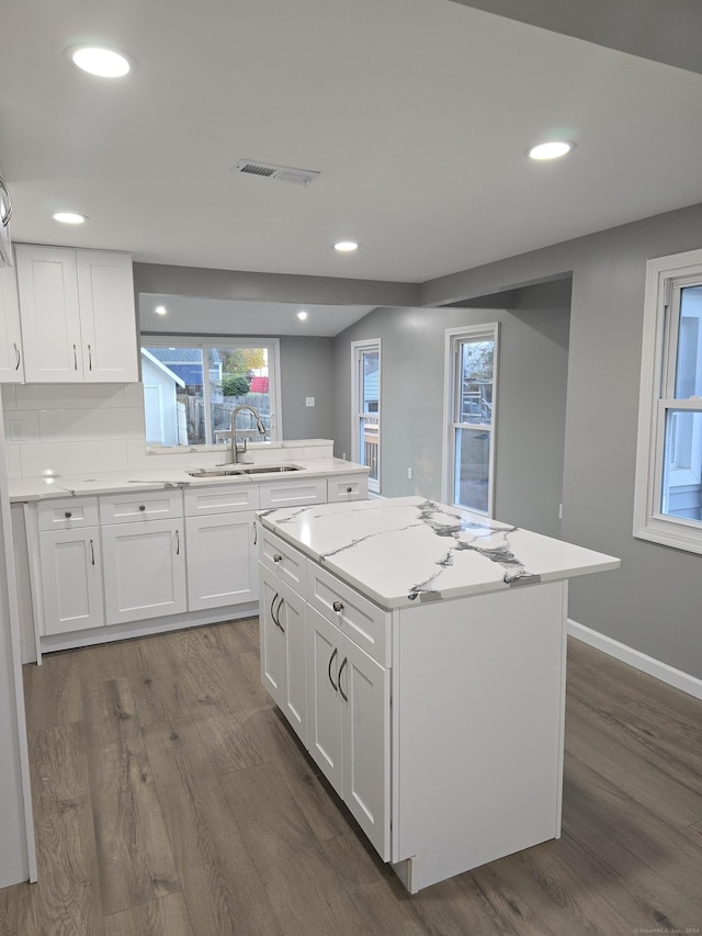 kitchen featuring white cabinets, a kitchen island, a sink, and light stone countertops