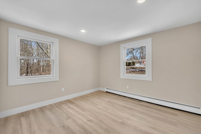 unfurnished room with a baseboard heating unit, light hardwood / wood-style floors, and a healthy amount of sunlight