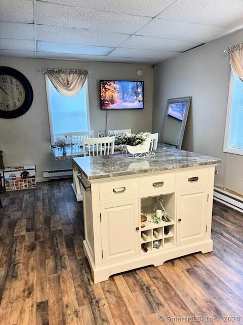 bar with a drop ceiling, dark wood-type flooring, baseboard heating, light stone counters, and white cabinetry