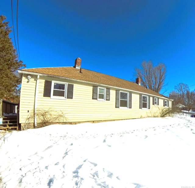 snow covered rear of property featuring a chimney