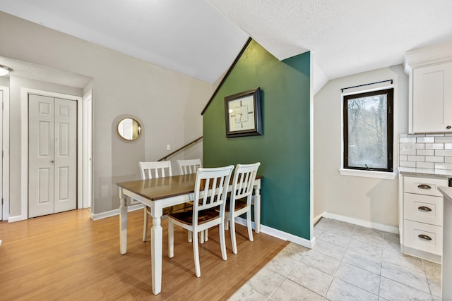 dining space featuring lofted ceiling, a textured ceiling, and light hardwood / wood-style flooring