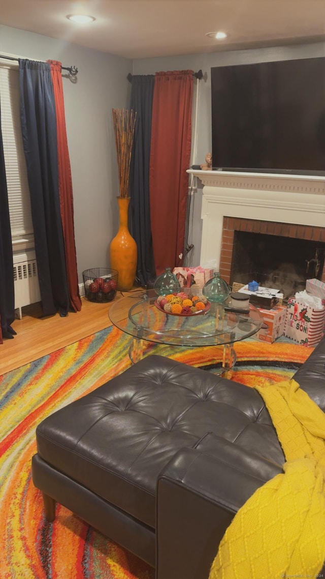 living room with radiator heating unit, a brick fireplace, and hardwood / wood-style floors