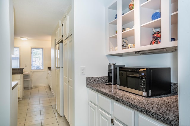 kitchen with white cabinets, white refrigerator, dark stone countertops, and light tile patterned flooring