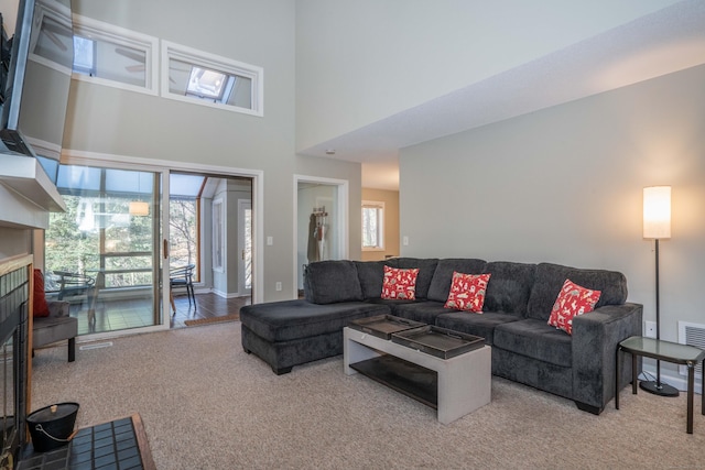 carpeted living room featuring a tiled fireplace and a towering ceiling