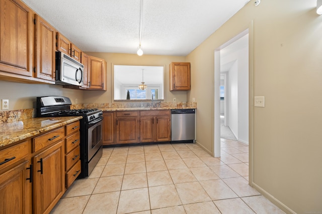 kitchen featuring light stone countertops, appliances with stainless steel finishes, a textured ceiling, and light tile patterned flooring