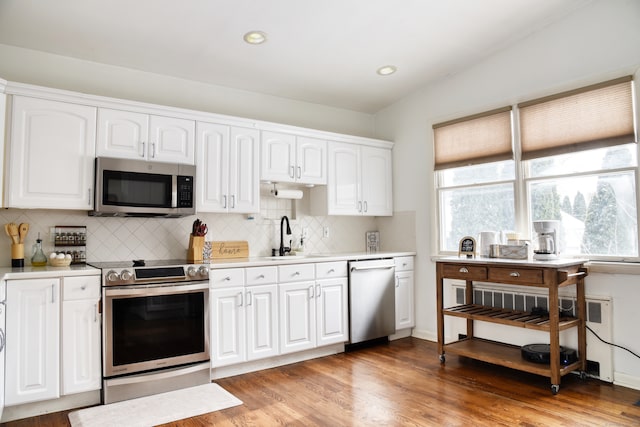 kitchen featuring sink, appliances with stainless steel finishes, white cabinetry, light hardwood / wood-style floors, and vaulted ceiling