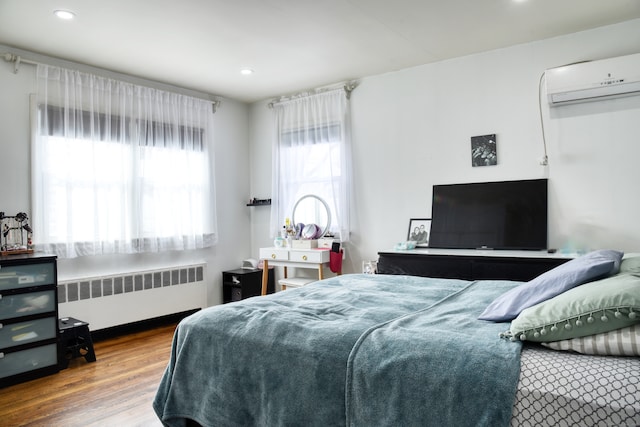 bedroom featuring a wall mounted AC, radiator, and hardwood / wood-style floors